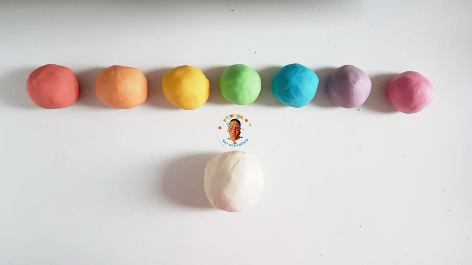 palline di pasta di sale di 7 colori. Da sinistra: rosso, arancione, giallo, verde, azzurro, lilla, rosa. In basso al centro: una palla più grossa al naturale (bianca)
