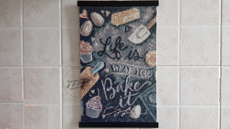 tela diamond painting con scritto "Life is what you bake it" sigillata e appesa al muro con stecche per poster